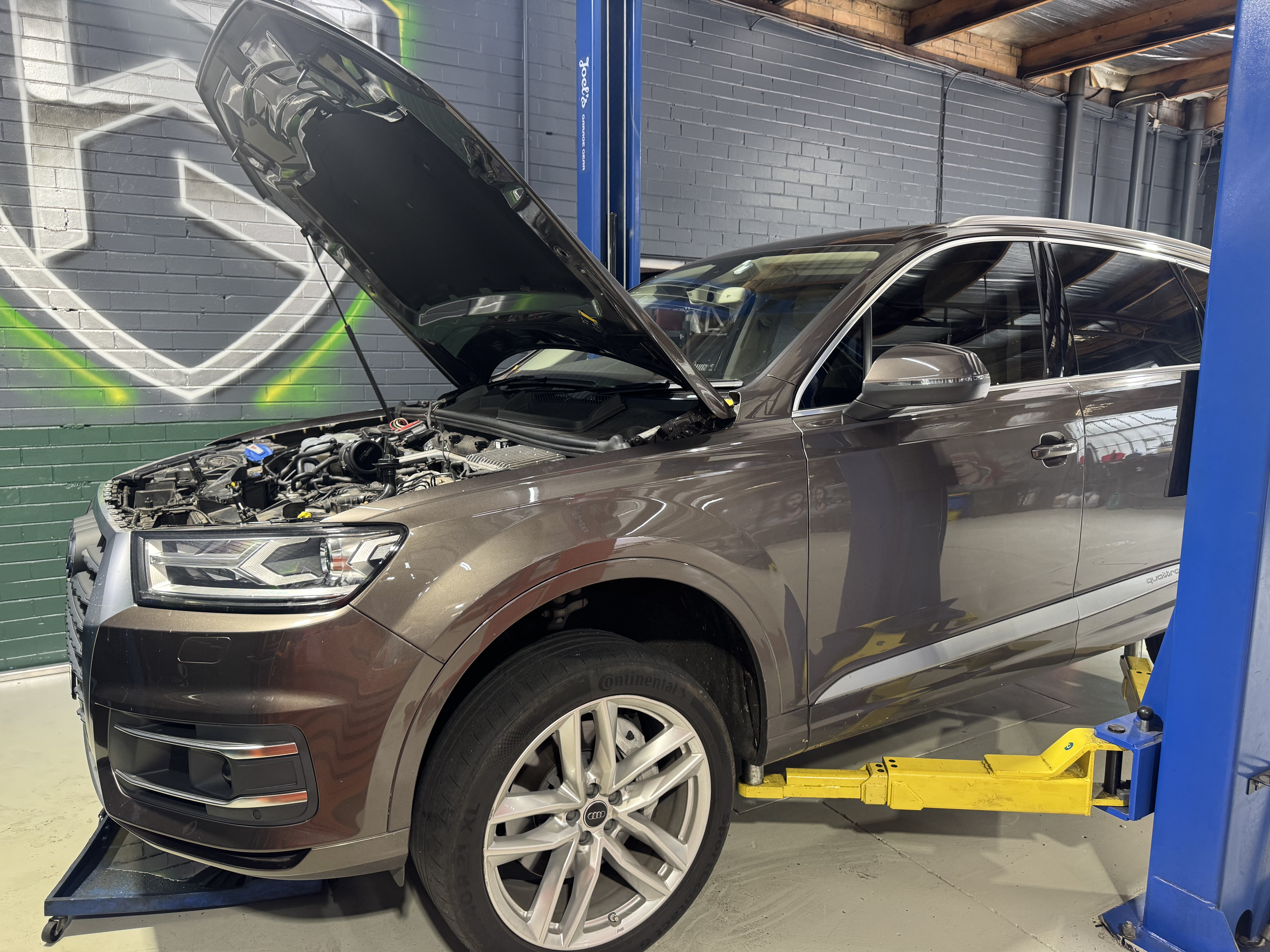 Brown Audi Q7 with hood open on lift — engine inspection