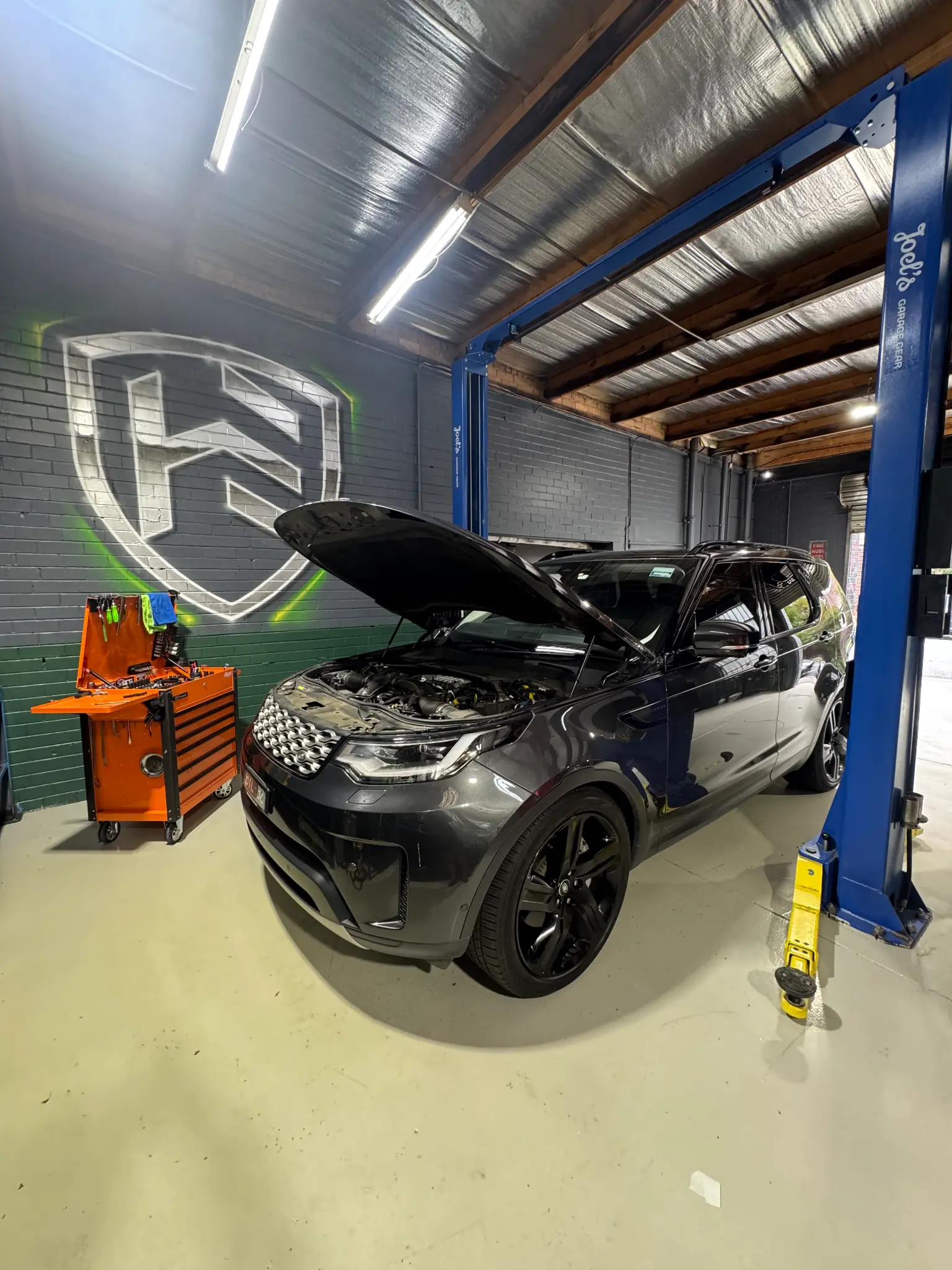 Dark grey Land Rover Discovery Sport with hood open, Hawthorn Eurotech shield logo on wall