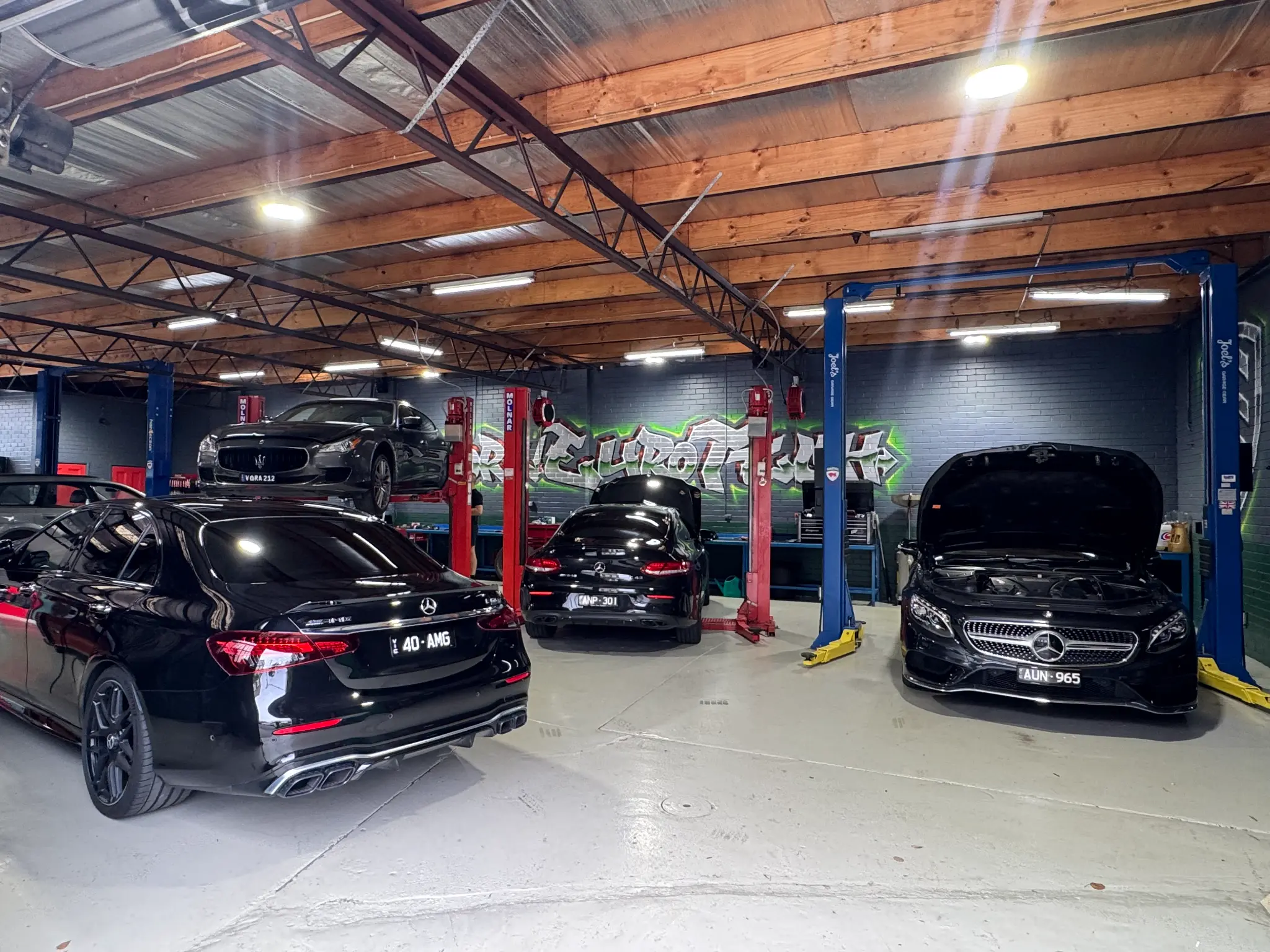 Three black Mercedes-AMG vehicles in Hawthorn Eurotech workshop with Maserati on lift