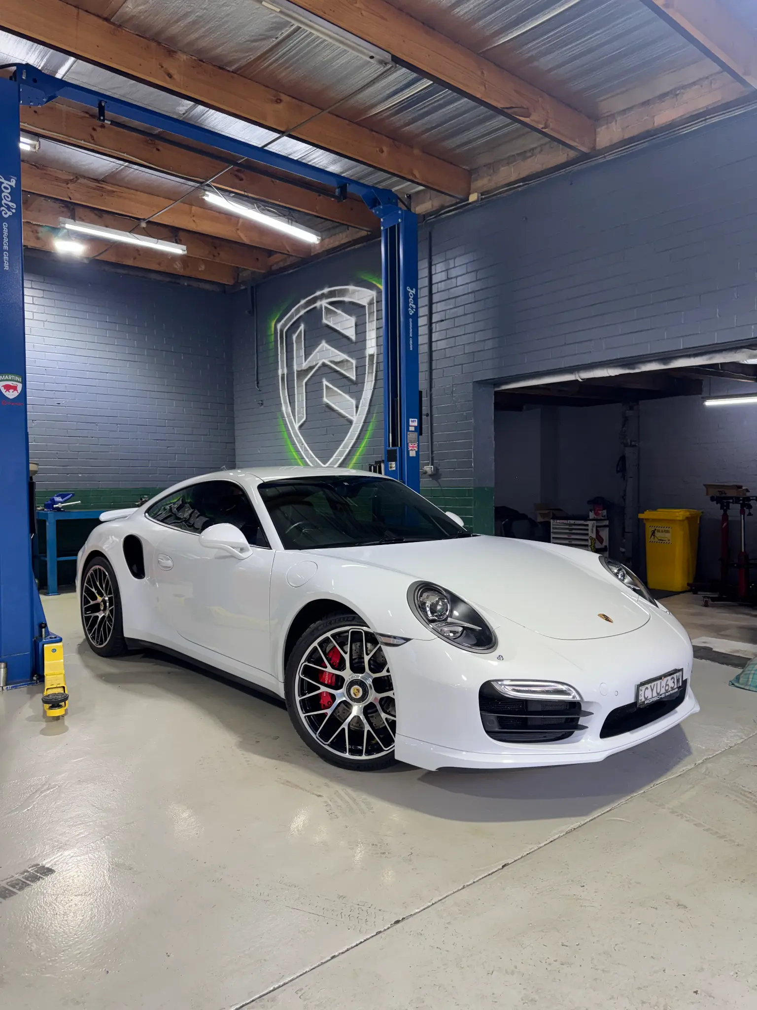 White Porsche 911 Turbo parked in Hawthorn Eurotech workshop with shield logo on wall