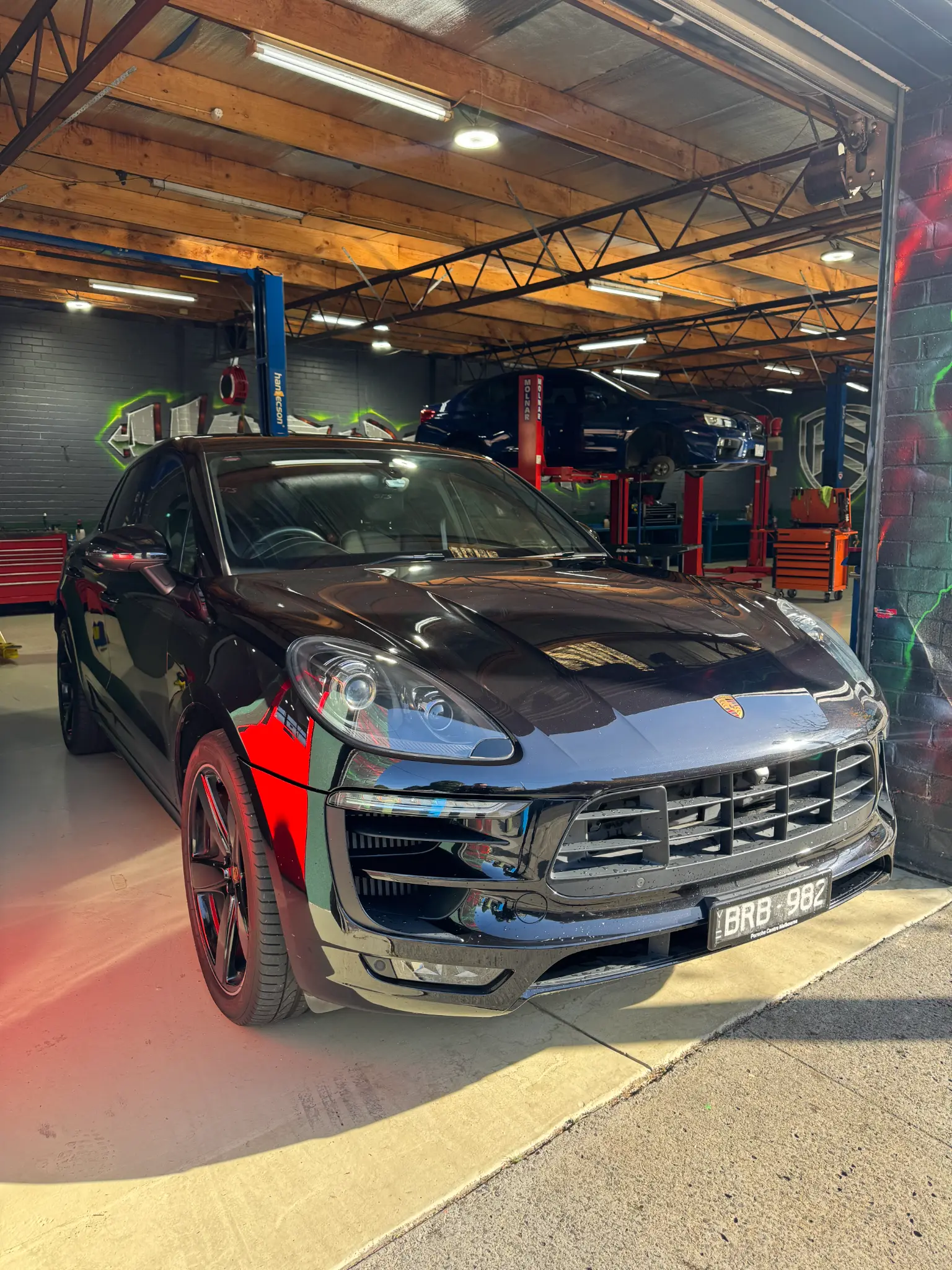 Black Porsche Macan at workshop entrance with busy service bay visible behind