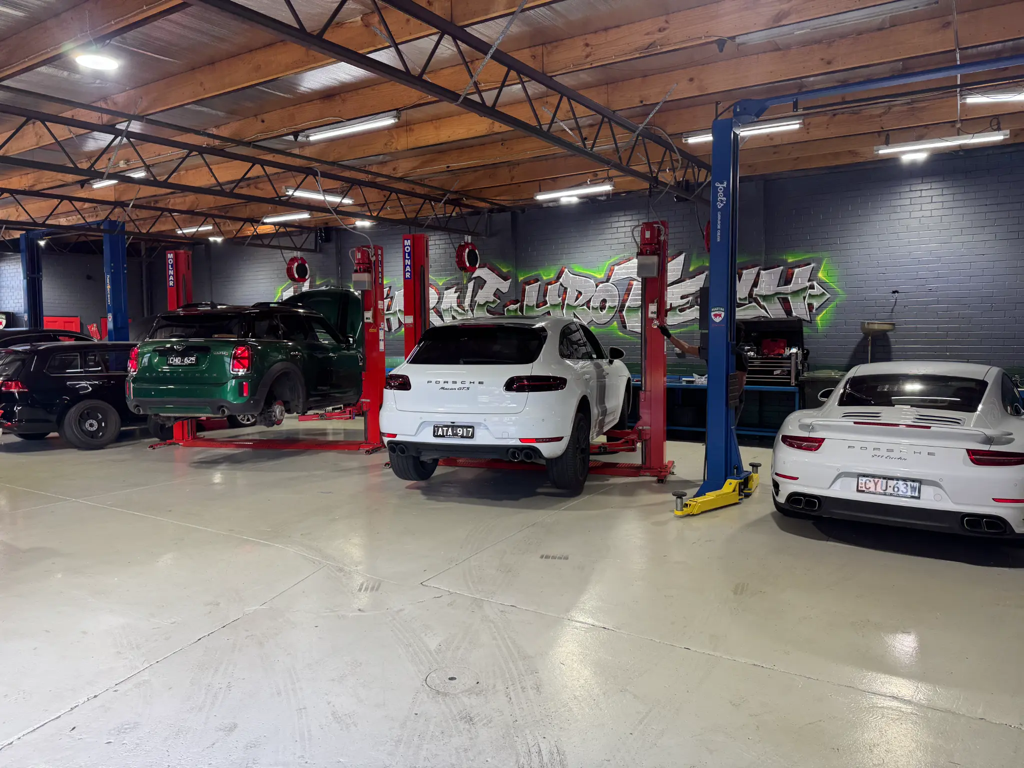 Green MINI, white Porsche Macan GTS and Porsche 911 Turbo in workshop